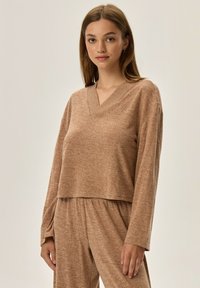 Brązowy, skrócony sweter z długim rękawem w miękkim, teksturowanym materiale z dekoltem w kształcie litery V, w zestawie z dopasowanymi dołami, na neutralnym tle.