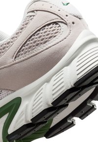 Zapatilla de color rosa claro con parte superior de malla, acentos de ante, media suela blanca y suela exterior negra texturizada con detalles en verde.