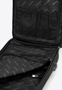 Interior de maleta negra con bolsillos de malla, compartimientos con cremallera y tela que muestra el nombre de la marca. Incluye un cable de carga USB.