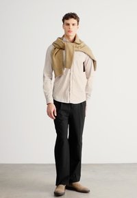 Svetlo pruhovaná béžová košeľa na gombíky, čierne nohavice a tenký tan sveter prehodený cez ramená; oblečené s béžovými topánkami. Jednoduchý, na mieru ušitý dizajn.