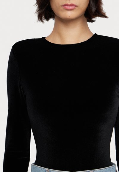 Svart fløyels bodysuit med lange ermer og rund hals, med en glatt tekstur og tettsittende design, kombinert med lyse denim-bukser.