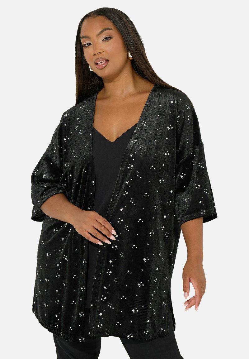 Musta samettinen kimono-tyylinen takki, jossa on V-pääntie, leveät hihat ja hajallaan olevia hopeisia tähtikoristeita. Sileä pinta, polven pituinen leikkaus.