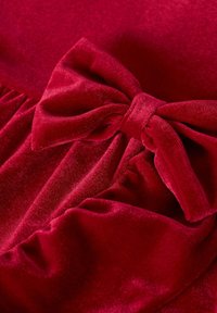 Tissu en velours rouge avec un nœud proéminent. La texture est douce et moelleuse, avec des drapés délicats dans le matériau environnant.