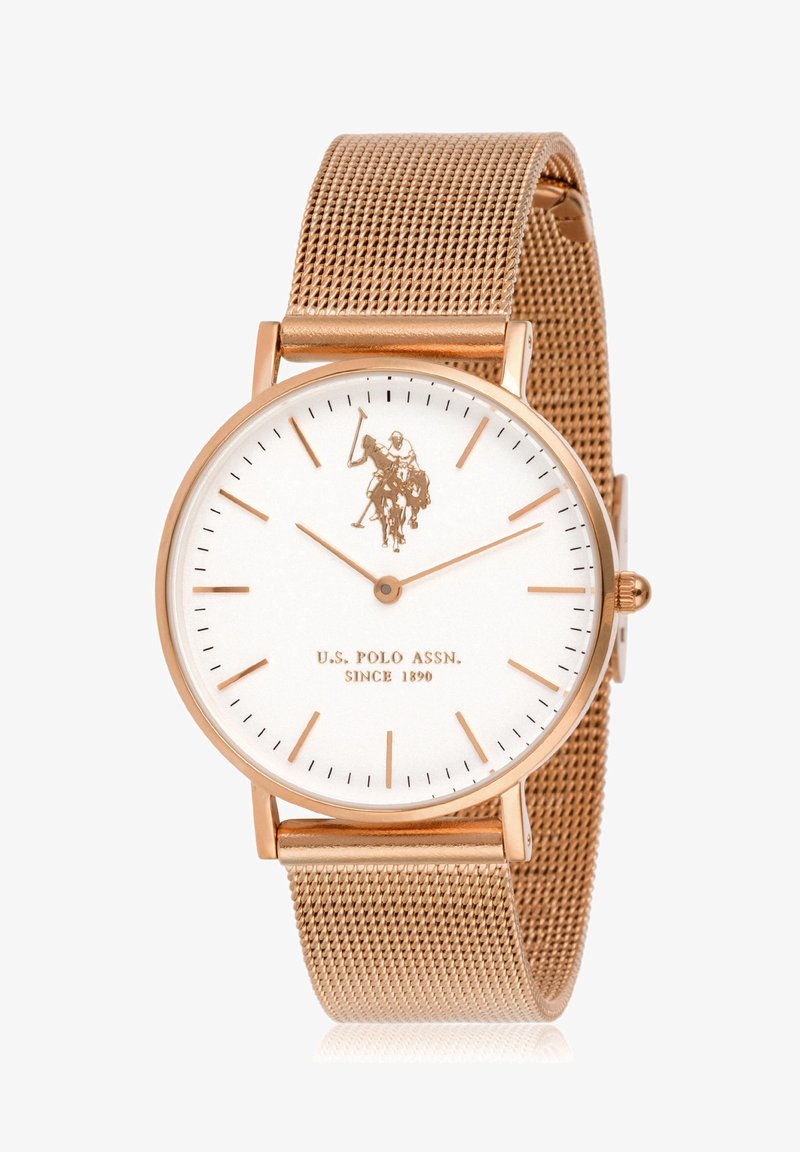 Quadrante bianco rotondo con accenti in oro rosa, cinturino a rete. Presenta un logo di un giocatore di polo, indicatori delle ore sottili e il testo del marchio in basso.