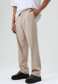 Beige op maat gemaakte broek met gladde stof, rechte snit en zijzakken, gecombineerd met zwarte veterlaarzen met dikke zolen.