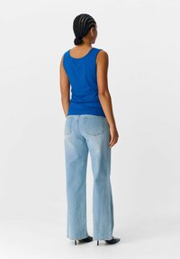 Top sin mangas azul con relieve combinado con jeans de pierna ancha de lavado claro. La parte superior presenta un escote redondeado. El atuendo se completa con tacones altos negros.