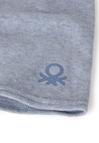 Jasnoniebieska tkanina o fakturze z delikatnym melanżowym wzorem, z akcentem w postaci ciemnoniebieskiego logo w dolnym rogu. Widoczne przeszycia na krawędziach.