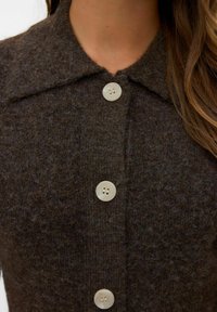 Cardigan en laine marron doté d'un col, de sept boutons et d'une finition texturée. Les boutons sont de couleur claire avec deux trous chacun.
