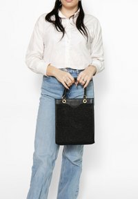 Borsa nera con superficie texturizzata, hardware dorato, manici superiori e forma rettangolare strutturata. La borsa presenta un accento liscio nella parte superiore.
