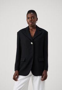 Blazer negru cu un singur buton în formă de floare, rever de tip notch și două buzunare frontale; textură netedă și croială ajustată.