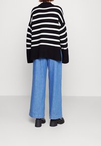 Black and white striped oversized knit sweater with a loose fit, paired with light blue wide-leg denim pants and chunky black heeled boots.