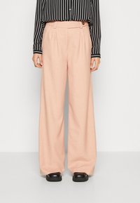 Světle růžové široké kalhoty s texturovanou tkaninou, předními sklady a bočním knoflíkem. V kombinaci s černo-bílou pruhovanou košilí.