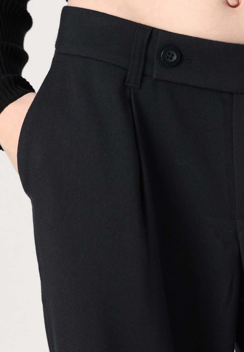 Pantalones negros ajustados con una textura suave, que presentan un cierre de botón, trabillas para cinturón y bolsillos laterales.