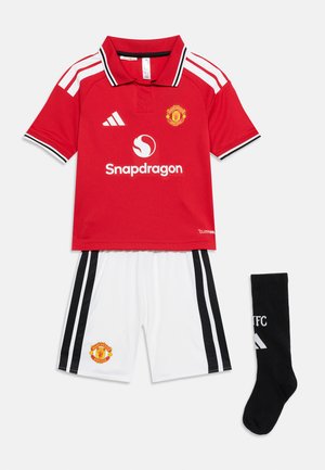 Manchester United focimez piros Adidas mezből, fehér rövidnadrágból fekete csíkokkal és fekete zokniból Adidas logóval.