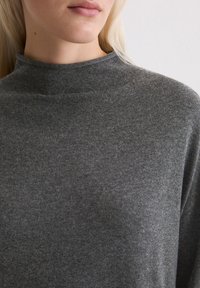 Pullover scuro a collo alto realizzato in morbido tessuto lavorato a maglia con una texture liscia. Presenta una silhouette aderente e un design minimalista.