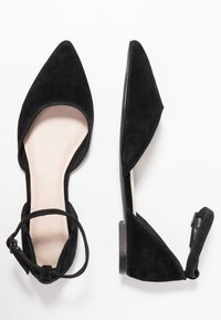 Ballerines pointues en daim noir avec un petit talon, côtés ouverts et bride à la cheville. Doublure intérieure lisse et design minimaliste.
