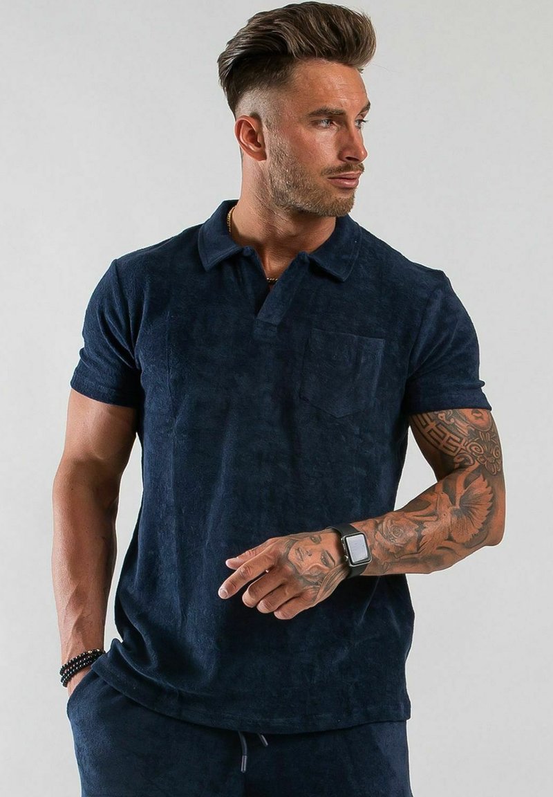 Mörkblå polo skjorta i strukturerad tygkvalitet, med krage, korta ärmar och en bröstficka. Enkel design med en avslappnad passform.