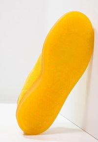 Klart gul sneaker-sula med en texturerad, mönstrad yta och en slät kant, med ett bikakesdesign för förbättrat grepp.