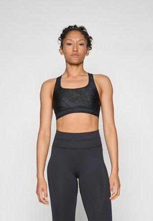 Svart sportsbh med teksturert mønster, brede stropper og et merket elastisk bånd, kombinert med høyt skjørtede svarte tights med logo.