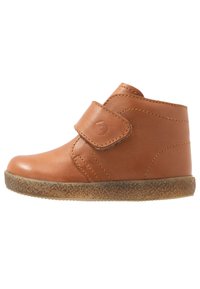 Bottine en cuir marron avec sangle Velcro, bout arrondi et semelle en caoutchouc marron texturée. Comprend des coutures jaunes et une surface lisse.