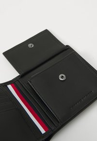 Zwart leren portemonnee interieur met meerdere kaartsleuven, drukknoopsluiting en een rood-wit-blauwe streepaccent aan één kant.