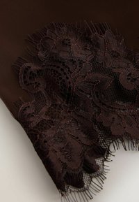 Tissu marron foncé avec application de dentelle florale détaillée comportant un filet complexe et des bords effilochés sur un fond lisse.
