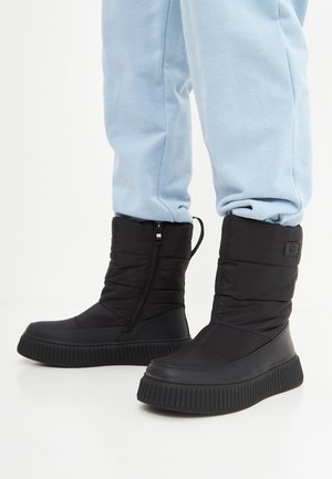 Bottines noires à la cheville, confortables avec une haute semelle en caoutchouc, dotées d'une fermeture éclair sur le côté et de détails cousus pour une apparence texturée.