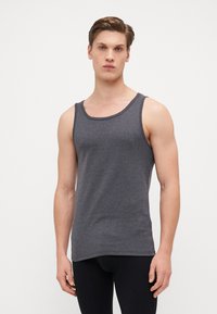 Szürke pamut ujjatlan felső, kerek nyakkal és széles karöltőkkel, puha tapintással és egyenes aljjal. Fekete leggings-szel viselve.