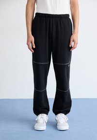 Sorte sweatpants med elastisk talje, med kontrasterende syninger og tapered manchetter, parret med hvide sneakers.