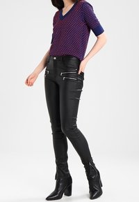 Černé skinny kalhoty z umělé kůže se stříbrnými zipovými detaily a přiléhavým střihem, zkombinované s krátkým rukávem vzorovaným topem v námořnické a červené barvě.