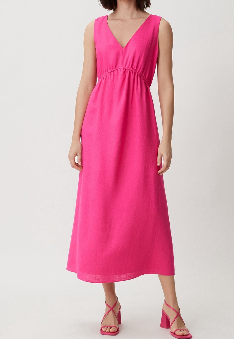 Femme portant une robe midi rose vif sans manches à encolure en V et des sandales à talons blocs assorties à lanières, debout devant un fond uni.
