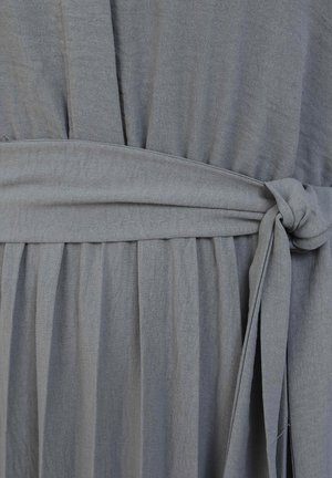 Gray fabric dress detail with gathered texture, waist tie, and overlapping pleats. Soft, lightweight material with a smooth finish.