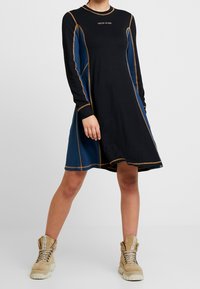 Långärmad klänning i svart och blått, med kontrasterande sömmar och en avslappnad passform. Har rund halsringning och logotyp vid br östet.