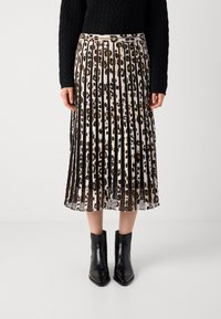 Vrouw in een geplooide midi-jurk met verticale luipaardprintstrepen, zwarte enkellaarsjes en een zwart kabelgebreid sweater.
