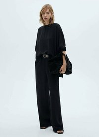 Top nero oversize con collo alto, abbinato a pantaloni neri larghi. Accessoriato con una borsa nera e sandali piatti. Tessuto morbido.