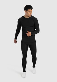 Schwarzes langärmliges Sportoberteil mit Raglanärmeln, kombiniert mit schwarzen, enganliegenden Leggings. Der Stoff wirkt glatt und dehnbar.