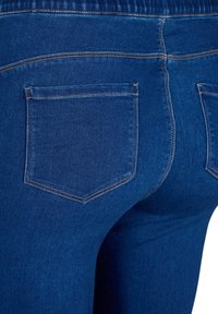Blue denim jeans featuring two rear pockets, visible stitching, and a stretchy waistband. Material has a smooth texture and dark wash.