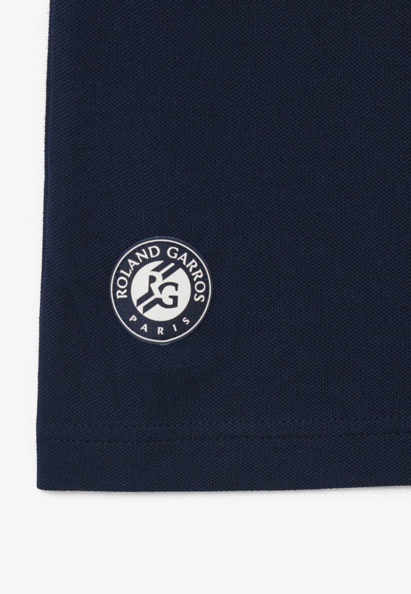 Logo Roland Garros Paris sur tissu texturé bleu marine, centré près du bord inférieur du tissu.