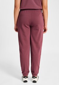 Bordowe spodnie dresowe z elastycznym pasem i ściągaczami. Wykonane z miękkiego materiału, o luźnym kroju, bez widocznych wzorów czy ozdób.