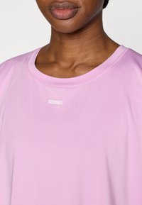 Αθλητική μπλούζα σε ανοιχτό ροζ χρώμα με στρογγυλή λαιμόκοψη, με λευκό λογότυπο "STRONGER" στο κέντρο. Λείο ύφασμα, κοντά μανίκια.