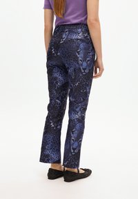 Pantaloni con stampa leopardata blu caratterizzati da un fit sartoriale e un design con gamba dritta. Il materiale ha una texture liscia, abbinati a delle ballerine nere.
