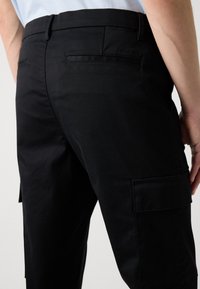 Zwarte cargobroek met een gladde textuur, een rechte snit, zijzakken en een discreet logo op de achterwaistband.