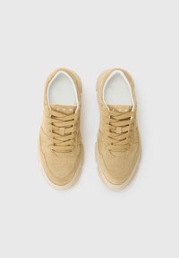Tan skinnesneakers med gummisåle, rund tå, perforerte detaljer på forsiden og flat snøring. Har "CPH" merke på tungen.
