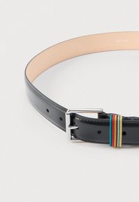 Cinturón de cuero negro con hebilla plateada, con un detalle de tela multicolor y cinco agujeros de ajuste. Acabado liso con interior beige.
