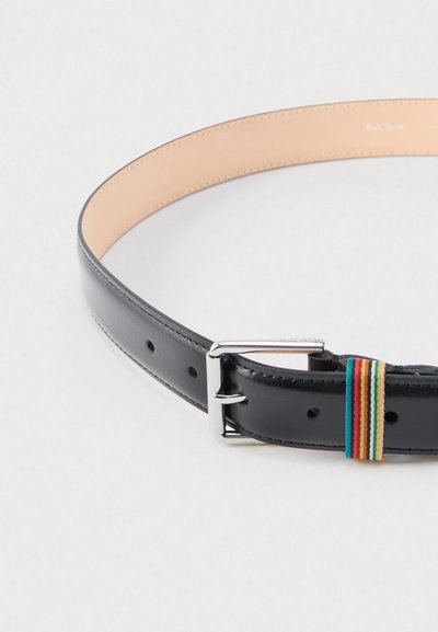 Juodas odinis diržas su sidabrine sagtimi, puoštas daugių spalvų audinio akcentu ir penkiomis reguliavimo skylutėmis. Lygus paviršius ir smėlio spalvos vidus.