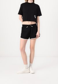 Svart kortärmad t-shirt med korta ärmar och en logo på vänster bröst, kombinerat med svarta shorts med dragsko och sidostrikar.