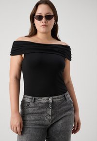 Μαύρο κορμάκι χωρίς ώμους από ελαστικό ύφασμα, με draped ντεκολτέ. Συνδυασμένο με ψηλόμεσα τζιν παντελόνια σε γκρι απόχρωση με όξινη πλύση.