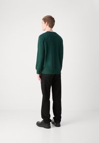 Donkergroene sweatshirt met een ronde halslijn en ribgebreide manchetten, gecombineerd met zwarte broeken. Soepele textuur met een casual pasvorm, gezien van achter.