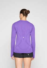 Long-sleeve purple athletic top featuring a smooth texture and subtle design accents; worn with black shorts.