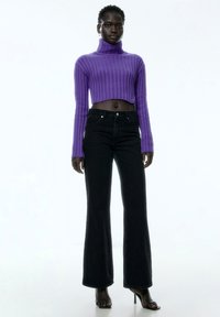 Paars geribbelde coltrui crop top gecombineerd met hoge zwarte flared jeans en zwarte blokhakken sandalen.